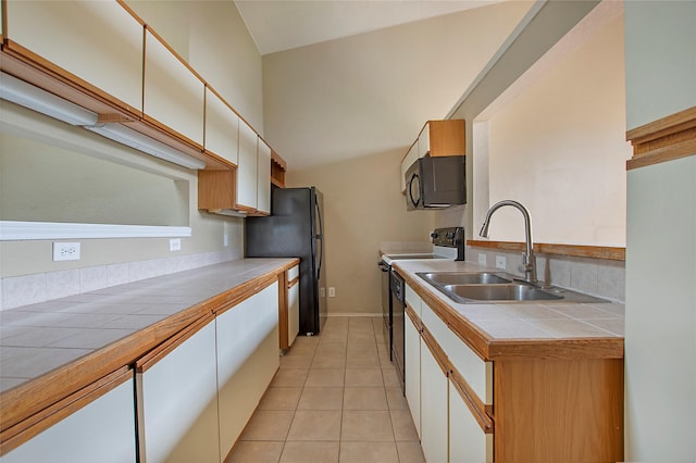 kitchen with a sink, light tile patterned floors, black appliances, tile counters, and white cabinetry