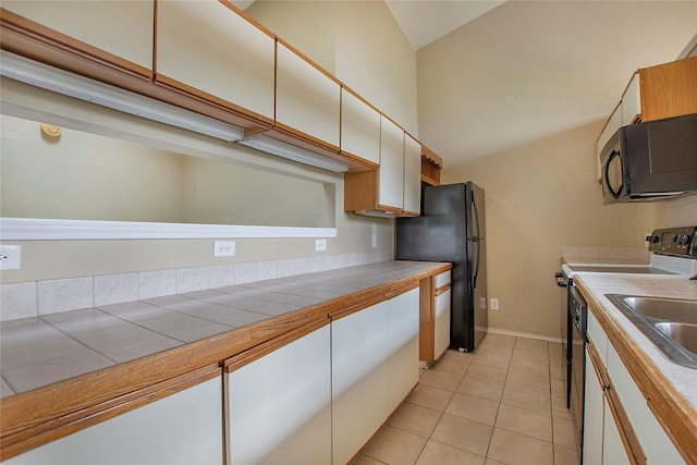 kitchen featuring a sink, tile counters, high vaulted ceiling, light tile patterned floors, and black appliances