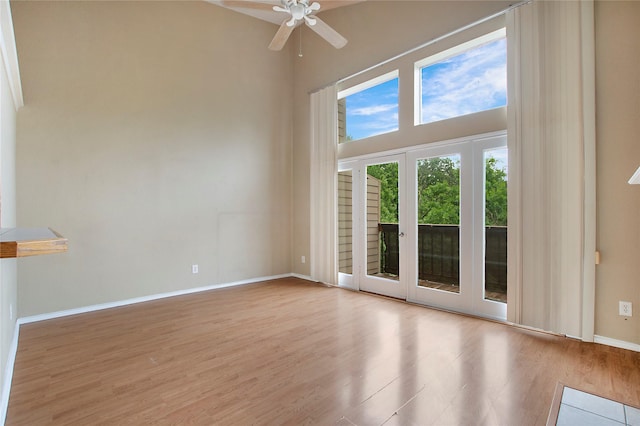 spare room featuring baseboards, a ceiling fan, a towering ceiling, and wood finished floors