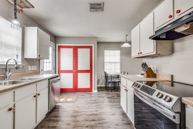kitchen with appliances with stainless steel finishes, a sink, light wood-type flooring, under cabinet range hood, and visible vents