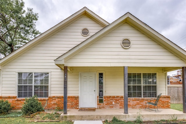 bungalow-style home featuring covered porch, brick siding, and fence