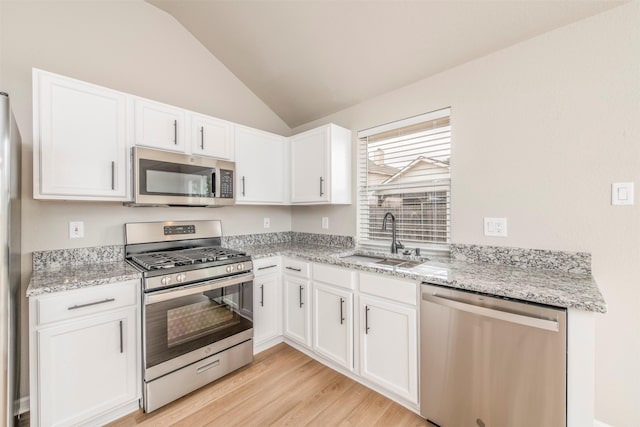 kitchen featuring light wood-type flooring, white cabinets, a sink, appliances with stainless steel finishes, and vaulted ceiling