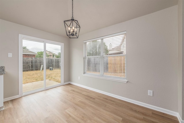 unfurnished dining area with baseboards, a notable chandelier, and light wood-style flooring