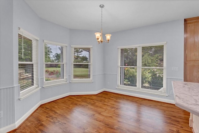 unfurnished dining area with baseboards, wood finished floors, and a notable chandelier