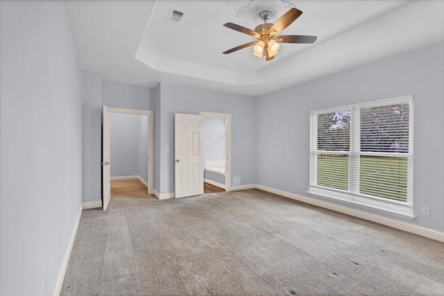 unfurnished bedroom with ceiling fan, carpet floors, baseboards, ensuite bathroom, and a tray ceiling
