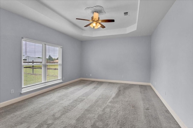 carpeted spare room with a raised ceiling, ceiling fan, baseboards, and visible vents
