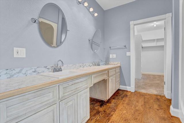 full bathroom with double vanity, baseboards, a sink, and wood finished floors