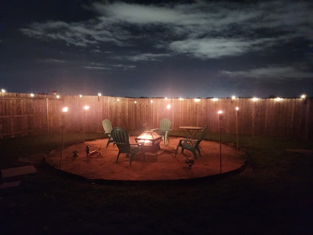 patio at night featuring a fire pit and fence