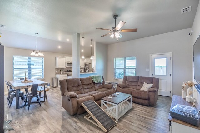 living room with visible vents, ceiling fan with notable chandelier, and light wood-type flooring