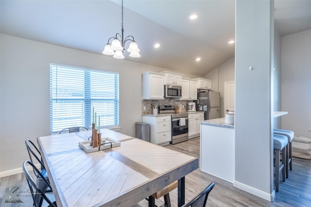 dining area featuring baseboards, a notable chandelier, lofted ceiling, and light wood-type flooring