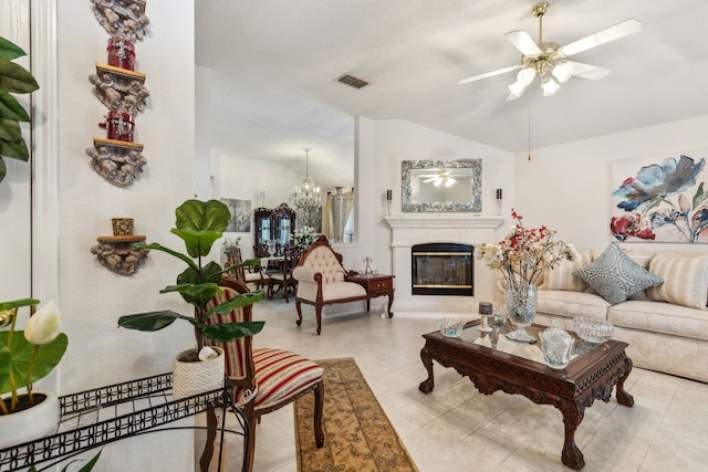 living area featuring visible vents, a glass covered fireplace, ceiling fan with notable chandelier, and vaulted ceiling