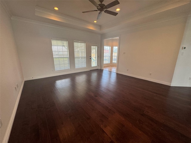 empty room with dark wood-style flooring, ceiling fan, a raised ceiling, baseboards, and ornamental molding