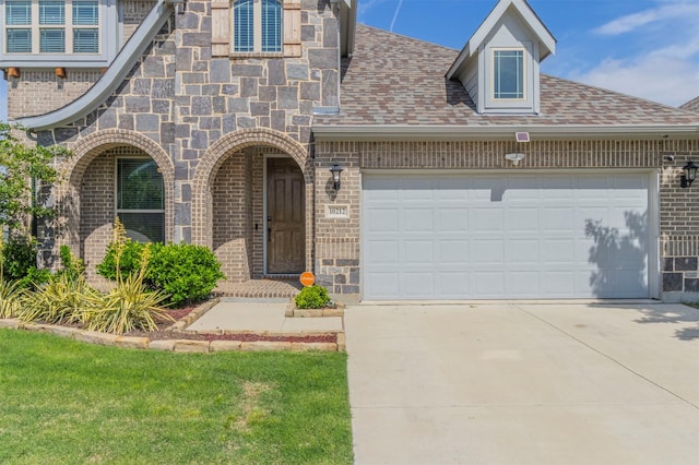 view of exterior entry with brick siding, a garage, a shingled roof, and concrete driveway
