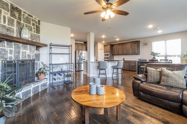 living area with a ceiling fan, dark wood finished floors, visible vents, and a fireplace