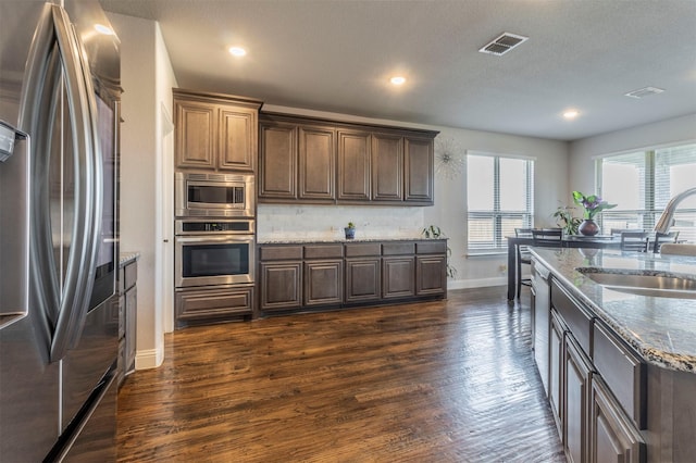 kitchen featuring visible vents, appliances with stainless steel finishes, dark wood finished floors, a sink, and baseboards