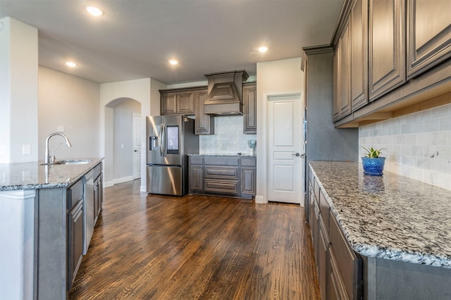 kitchen with appliances with stainless steel finishes, arched walkways, a sink, custom exhaust hood, and dark wood-type flooring