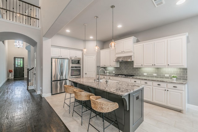 kitchen with visible vents, arched walkways, stainless steel appliances, light stone counters, and under cabinet range hood