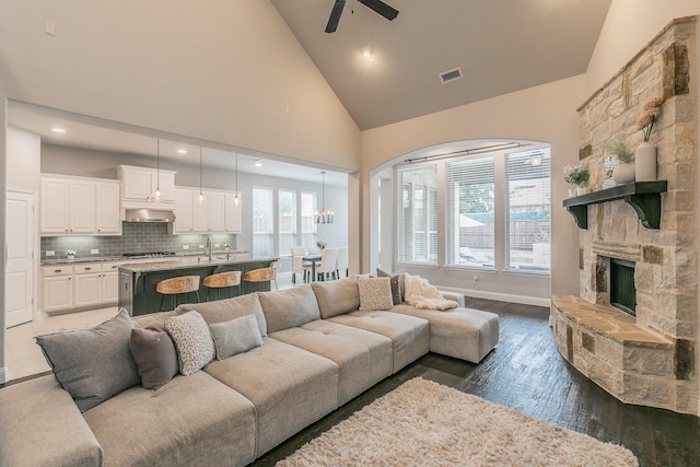 living room featuring visible vents, dark wood-style flooring, a fireplace, ceiling fan, and high vaulted ceiling