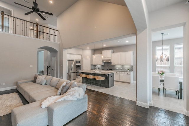 living room with arched walkways, baseboards, ceiling fan with notable chandelier, and a towering ceiling