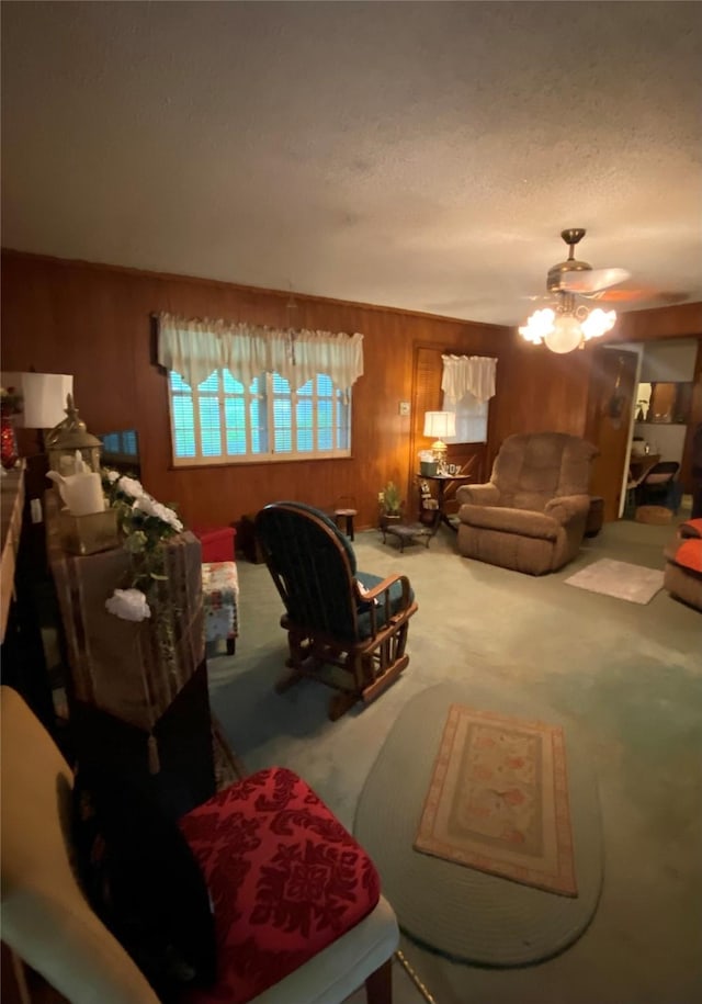 carpeted living area with ceiling fan, wood walls, and a textured ceiling