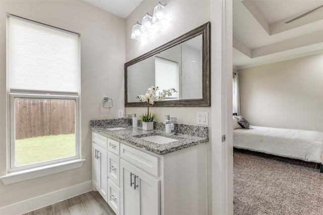 ensuite bathroom with a sink, ensuite bath, double vanity, baseboards, and wood finished floors