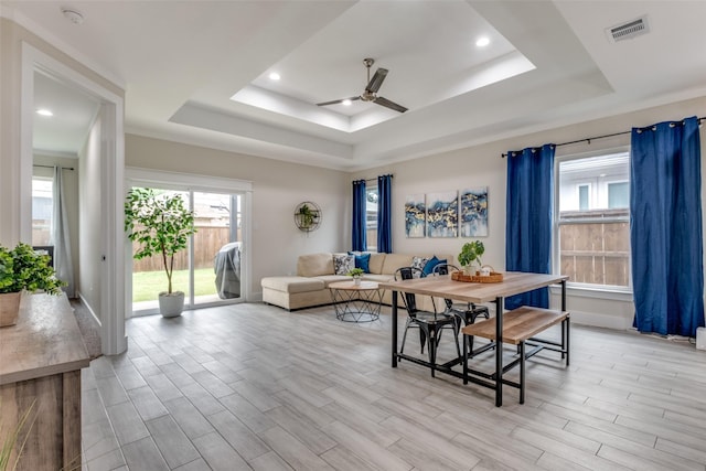 dining room featuring light wood finished floors, a ceiling fan, baseboards, a tray ceiling, and visible vents