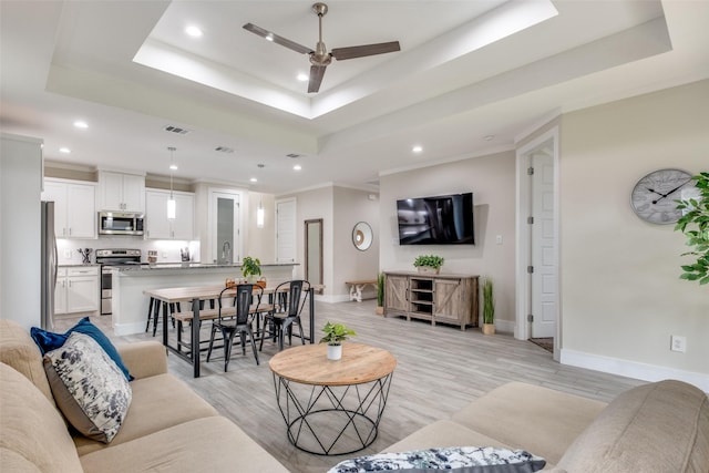 living room with a ceiling fan, visible vents, a raised ceiling, light wood-style floors, and recessed lighting