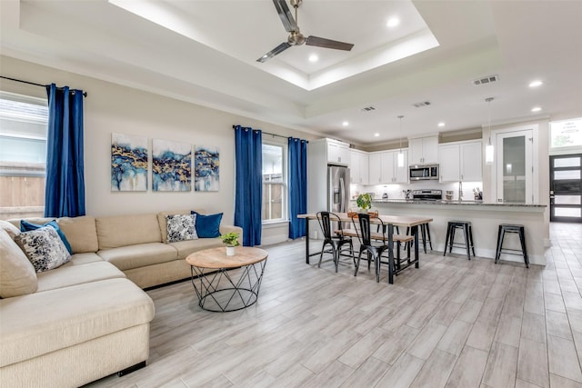 living room featuring ceiling fan, visible vents, a healthy amount of sunlight, and a raised ceiling