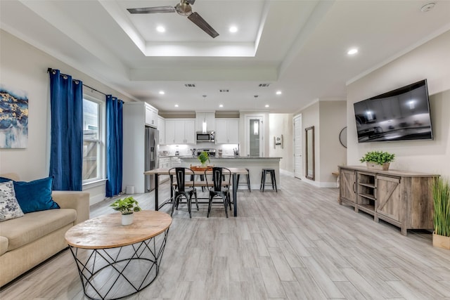 living area with a ceiling fan, recessed lighting, light wood-type flooring, a tray ceiling, and visible vents