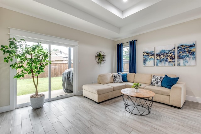 living area with baseboards, a tray ceiling, and light wood-style floors