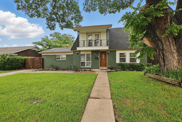 view of front of house featuring fence, roof with shingles, a front lawn, and a balcony