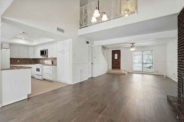 unfurnished living room with visible vents, wood finished floors, a high ceiling, a tray ceiling, and a ceiling fan