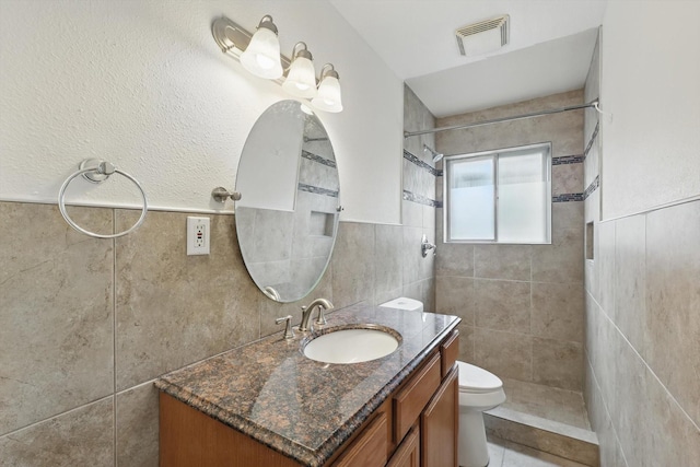 full bath with visible vents, tile walls, vanity, toilet, and tiled shower