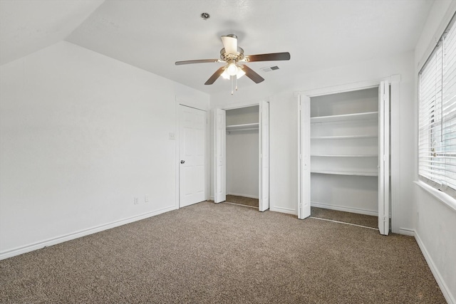 unfurnished bedroom featuring visible vents, carpet floors, multiple closets, baseboards, and vaulted ceiling