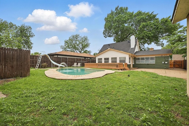 view of swimming pool with a wooden deck, a fenced in pool, a fenced backyard, a yard, and a water slide