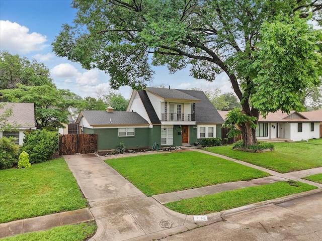view of front of property with fence, a balcony, a front yard, roof with shingles, and driveway