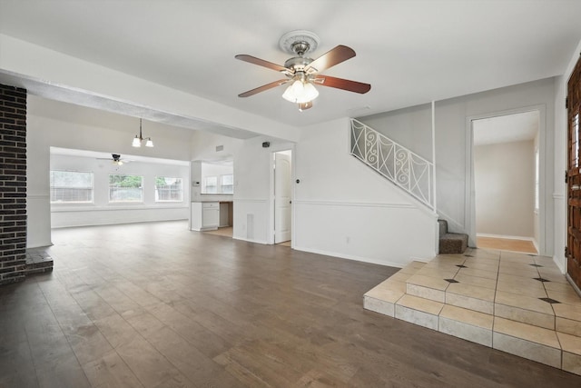 unfurnished living room with stairs, a ceiling fan, and wood finished floors