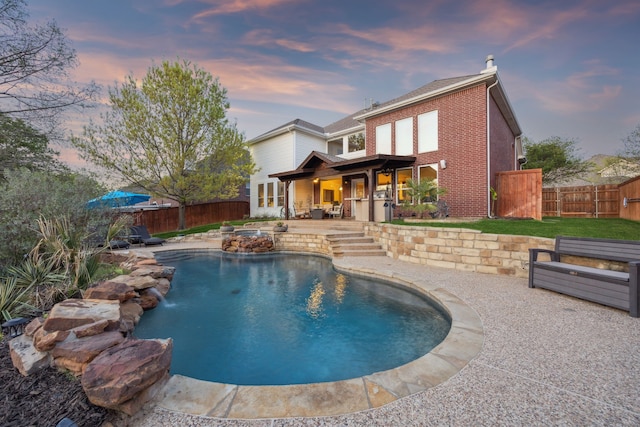 back of property at dusk featuring a fenced backyard, a patio area, a fenced in pool, and brick siding