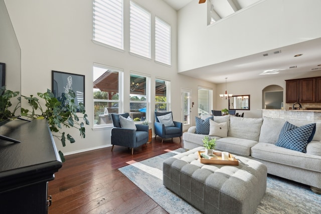 living area with a notable chandelier, dark wood-style floors, a wealth of natural light, visible vents, and a high ceiling