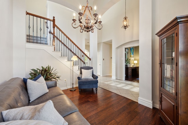living room with an inviting chandelier, wood-type flooring, high vaulted ceiling, baseboards, and arched walkways
