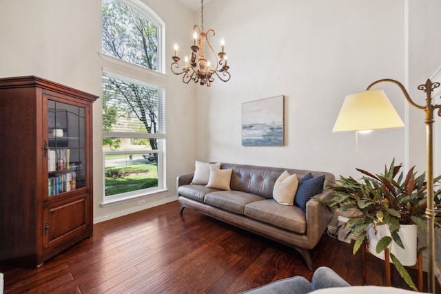 living area featuring an inviting chandelier, baseboards, a towering ceiling, and dark wood-style floors