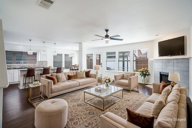 living room with a ceiling fan, visible vents, dark wood finished floors, and a fireplace