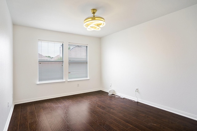 empty room featuring baseboards, an inviting chandelier, and dark wood-style floors