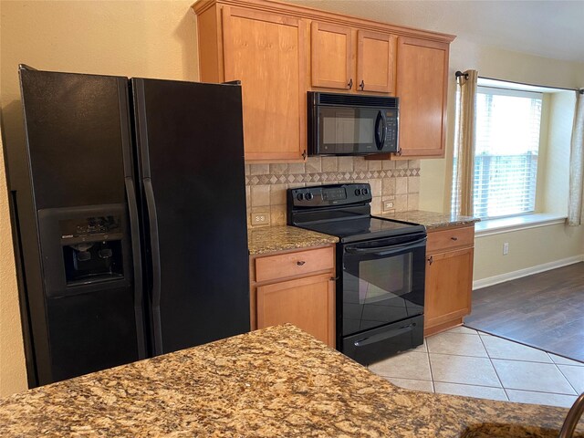 kitchen featuring tasteful backsplash, light stone countertops, light tile patterned floors, baseboards, and black appliances