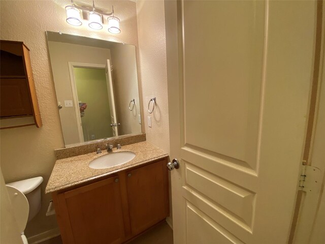 half bath featuring toilet, a textured wall, and vanity
