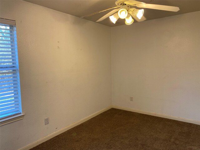 empty room with dark colored carpet, a ceiling fan, and baseboards