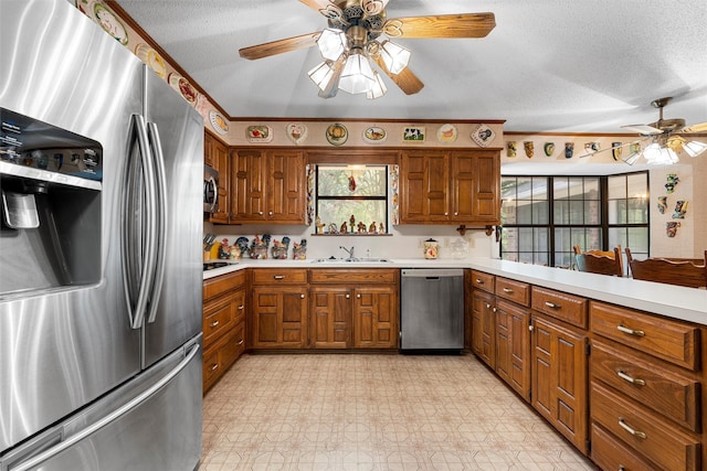 kitchen with brown cabinets, appliances with stainless steel finishes, a sink, light countertops, and a ceiling fan