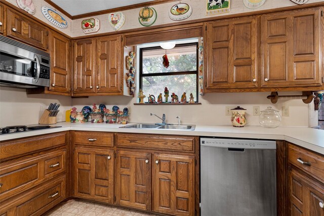 kitchen featuring light countertops, appliances with stainless steel finishes, brown cabinetry, and a sink