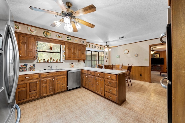 kitchen featuring a ceiling fan, brown cabinets, a sink, a peninsula, and stainless steel appliances