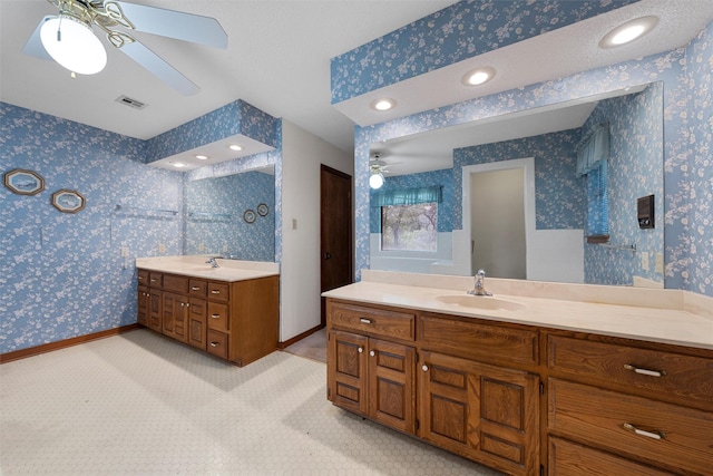 full bathroom with a sink, a ceiling fan, wallpapered walls, and two vanities
